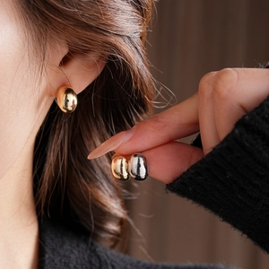 Close-up of minimalist gold and silver bean-shaped earrings on model with high gloss finish