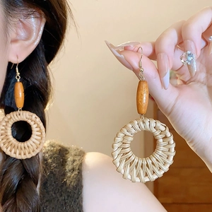 Close-up of bohemian style earrings featuring a wooden bead and round rattan woven pendant