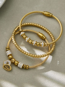 Détail de bracelets torsadés en acier doré 18 carats et d'un pendentif cœur