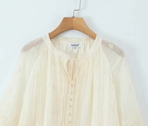 Détail d'une chemise crème à manches longues avec broderie florale et texture plissée