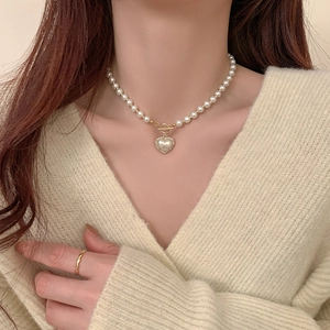 Detail of heart pendant necklace with pearls and golden OT buckle on elegant model