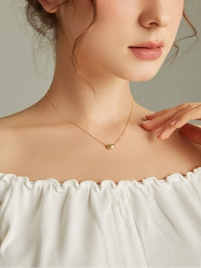 Macro shot of a golden bean pendant necklace on model collarbone with polished finish