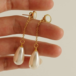Détail de boucles d'oreilles dorées avec longue chaîne et perle goutte blanche