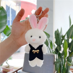 Detailed close-up of a white plush rabbit keychain with a black vest and gold bow detail