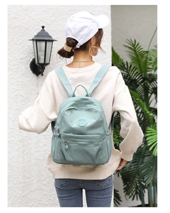 Close-up of a mint green nylon backpack with multiple zippered pockets and durable straps