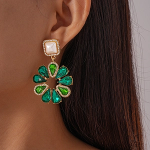 Dettaglio orecchini vintage a fiore con gemme verdi e perla su modella reale