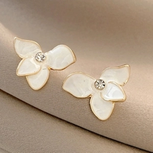 Close-up of elegant flower stud earrings with cream petals and gold edges on silk
