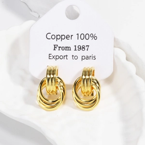 Close-up of gold layered hoop earrings on a shell stand showing 100% Copper label