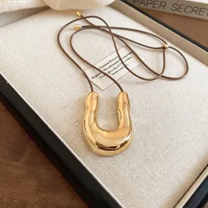 Collana con ciondolo a U dorato irregolare e cordino lungo marrone su un vassoio