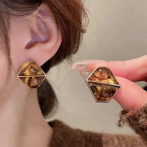 Detail view of amber resin hexagonal earrings with golden trim on model and hand