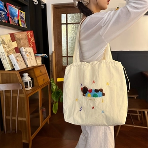 Detail of cream canvas tote bag featuring colorful embroidery and drawstring closure
