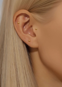 Detailed view of three gold star-shaped stud earrings worn on the earlobes and cartilage