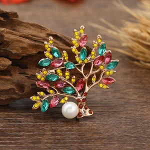 Golden tree of life brooch with colorful rhinestones and a white pearl on wood background