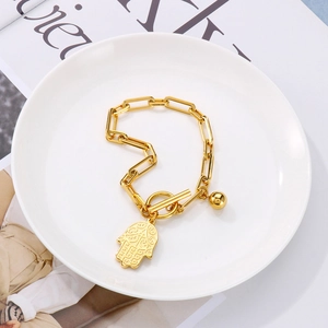 Detail of gold chunky chain bracelet with Hamsa palm and bead charms on a white plate