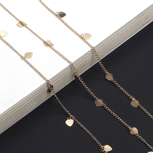Detail of gold eyewear chain with heart-shaped sequins on a minimalist dual-tone background