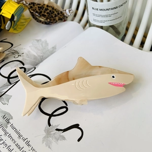 Detail of cream shark-shaped acetate hair claw clip on magazine with plants
