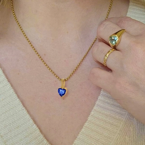Close-up of a gold chain necklace featuring a blue heart-shaped zircon pendant