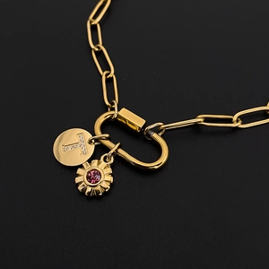Macro view of gold carabiner necklace with sparkling letter T charm and purple stone flower