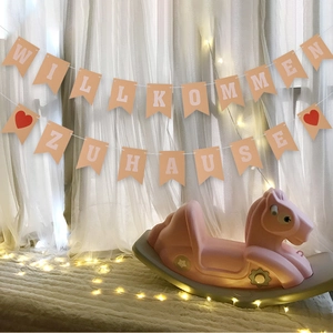 Pink rocking horse and German Welcome Home banner with Willkommen Zuhause text and lights