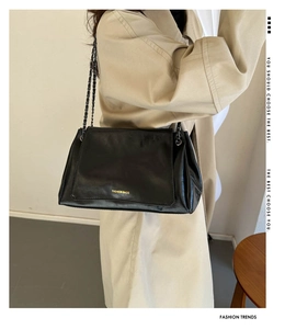 Close-up of a black leather chain shoulder bag with minimalist flap design and text