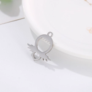 Silver cartoon devil pendant with wings and heart cutout on a white ceramic plate
