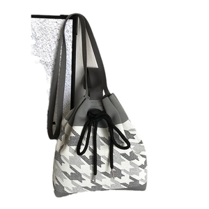 Knitted houndstooth drawstring bucket bag with black strap and gray woven texture