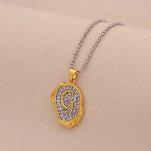 Macro view of gold letter G pendant necklace with pavé zircons on soft beige background