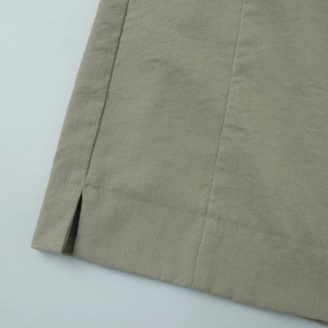 Detailed close-up of olive green linen-cotton fabric texture with side slit and stitching