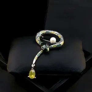 Detailed view of a silver snake brooch featuring green enamel, pearl, and yellow zircon