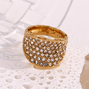 Vue macro d'une bague concave dorée à l'or 18K avec cristaux sur surface blanche