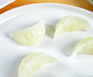Close-up of four realistic miniature dumplings with detailed pleats on a white plate