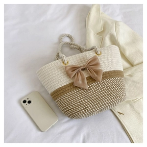 Close-up of a two-tone woven straw tote bag with a beige bow and rope handles