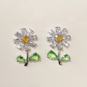 Macro detail of daisy flower stud earrings with crystal petals and green leaf accents