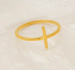 Close-up of a minimalist gold cross ring on white silk fabric background
