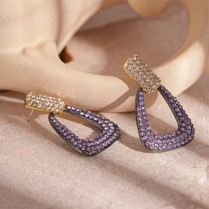 Macro shot of gold geometric triangle earrings with purple and white crystals detail