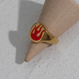 Detail of a gold stainless steel signet ring with a red enamel flame pattern