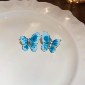 Close-up of blue butterfly enamel stud earrings with zircon on a white ceramic tray