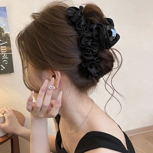 Detail of a large black satin pleated hair claw clip worn on a low bun hairstyle