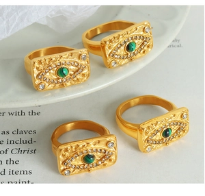 Close-up of four gold Evil Eye rings with green stones and zircons on a white plate