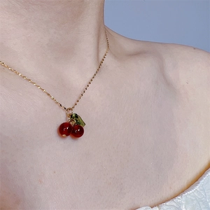 Close-up of red cherry pendant with green leaf on a gold chain worn by a model