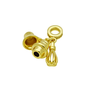 Macro detail of gold plated charms with whisk, bell, and cone pendant on white background