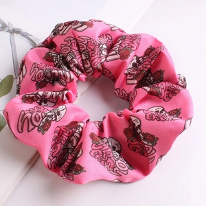 Detail of pink fabric scrunchie with skull, rose, and love patterns on white background