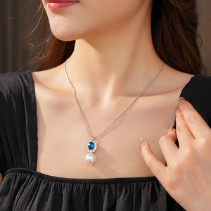 Dettaglio collana argento vintage con gemma blu e perla bianca indossata da modella