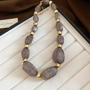 Detail of chunky acrylic irregular taupe glitter beads with gold spacers on a display tray