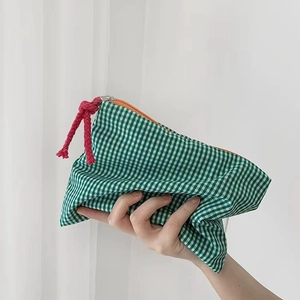 Green checkered makeup bag with orange zipper and red cord knot held in hand