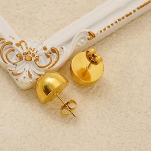 Detail view of golden semi-sphere stud earrings on beige textured fabric and vintage frame