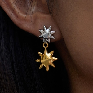 Macro shot of sun-shaped earrings in polished gold and silver tone stainless steel