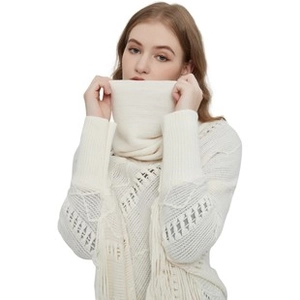 Close-up of cream-white knit poncho texture showing high collar and fringe detail