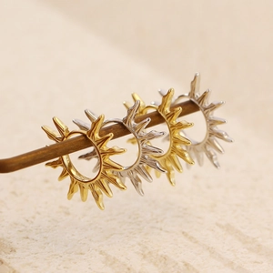 Detail of sunburst earrings in gold and silver finish hanging on a wooden stick