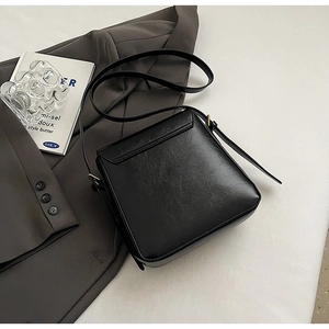 Detail view of the black textured leather square crossbody bag on a grey suit jacket